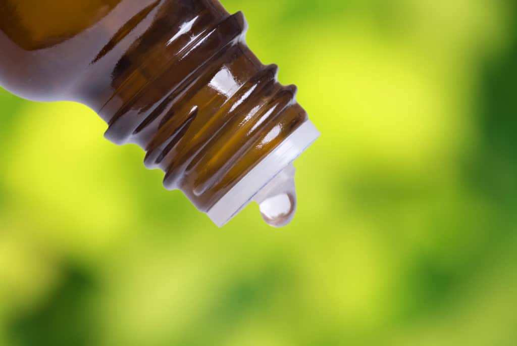 Macro shot of a bottle with drop, with fresh foliage in the background. Focus on bottle